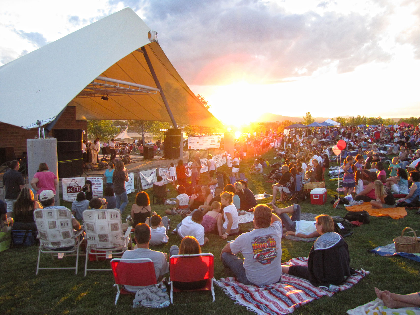 Large group of people sitting on the lawn at Clement Park during an event watching a performance.