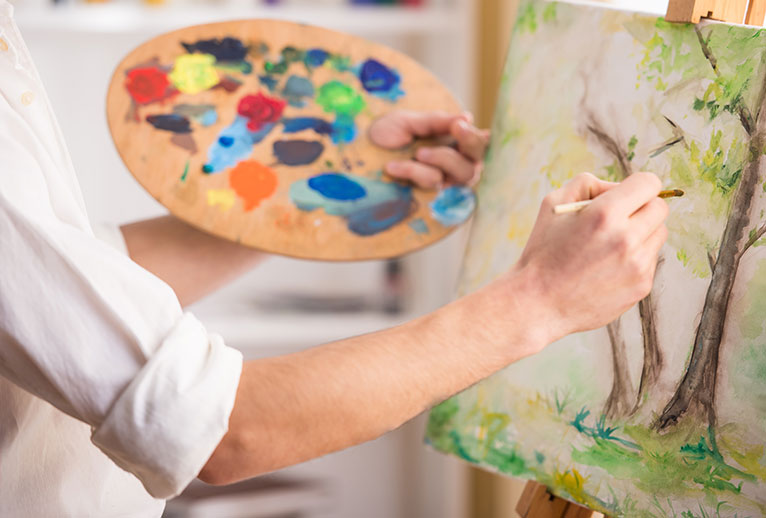 Painter holding a palate while painting onto a canvas.