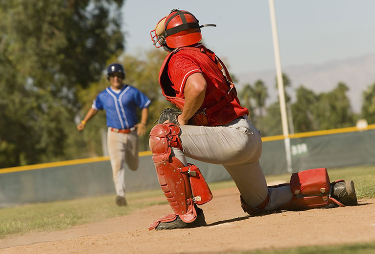 A catcher on a softball field watching a player run toward him.