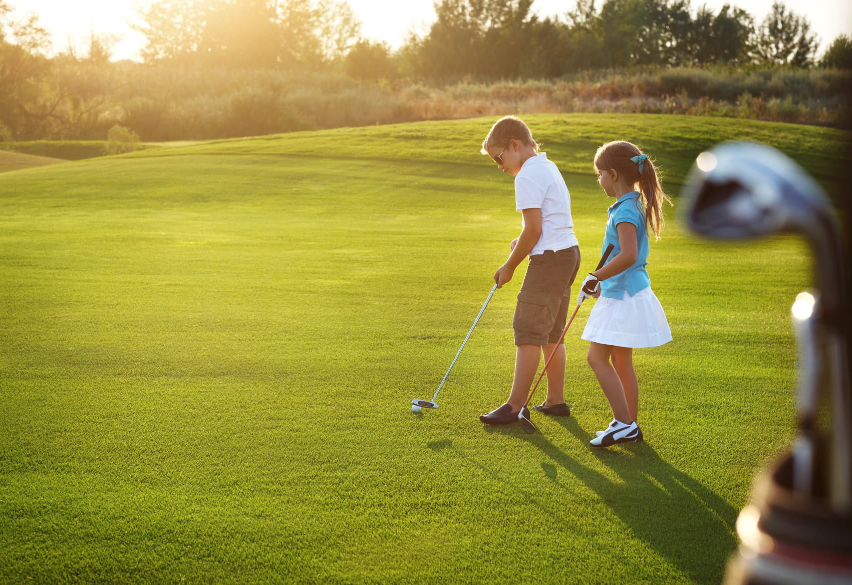 Casual kids at a golf field holding golf clubs Casual kids at a golf course holding golf clubs. Sunset