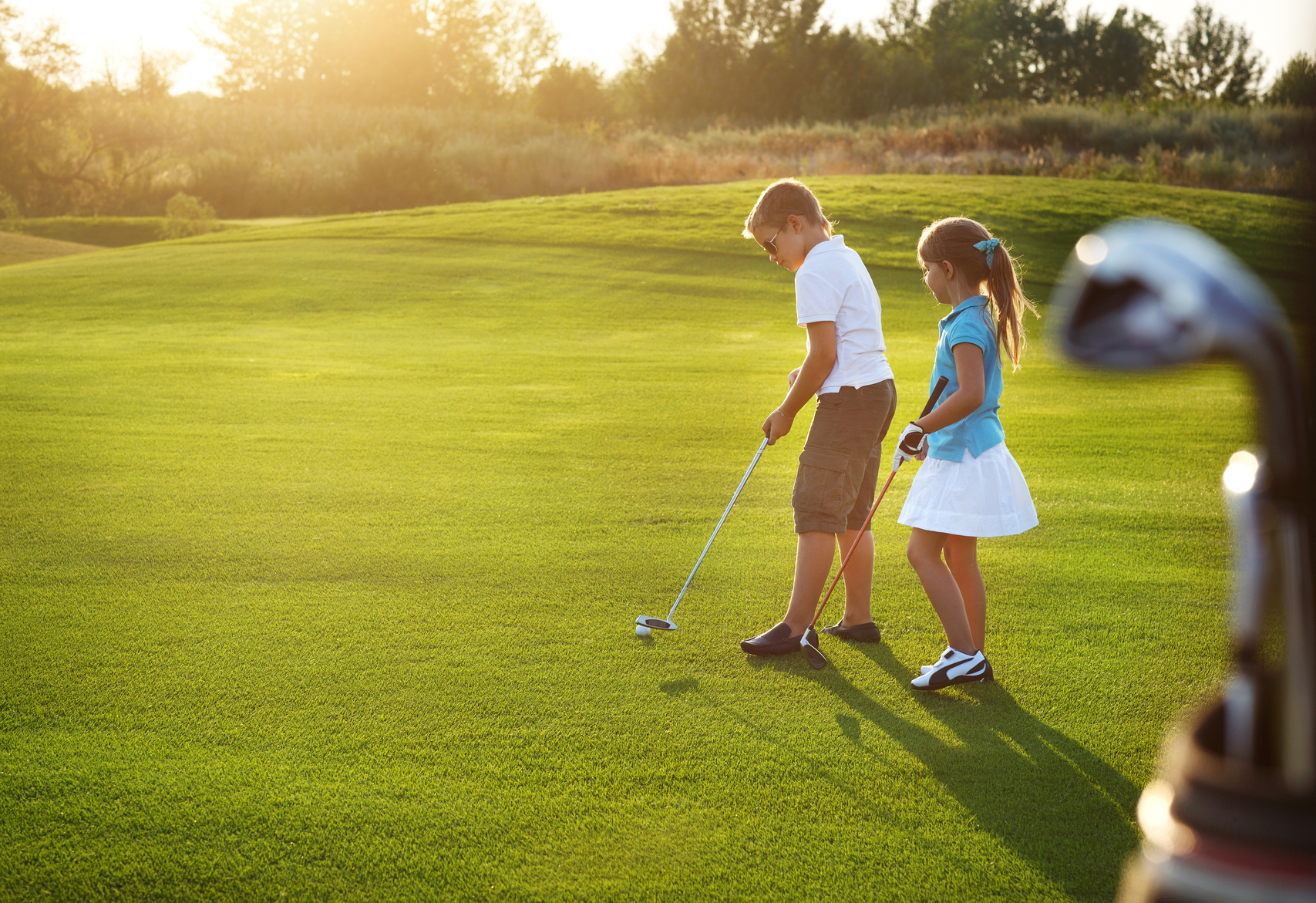 Casual kids at a golf course holding golf clubs. Sunset