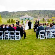 A group of people sitting on the lawn watching a wedding take place.