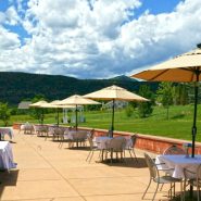 An outdoor patio set up with tables, chairs and umbrellas for a wedding reception with mountain views in the background.
