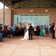 A bride and groom standing at the entry of the building surrounded by their wedding attendants.
