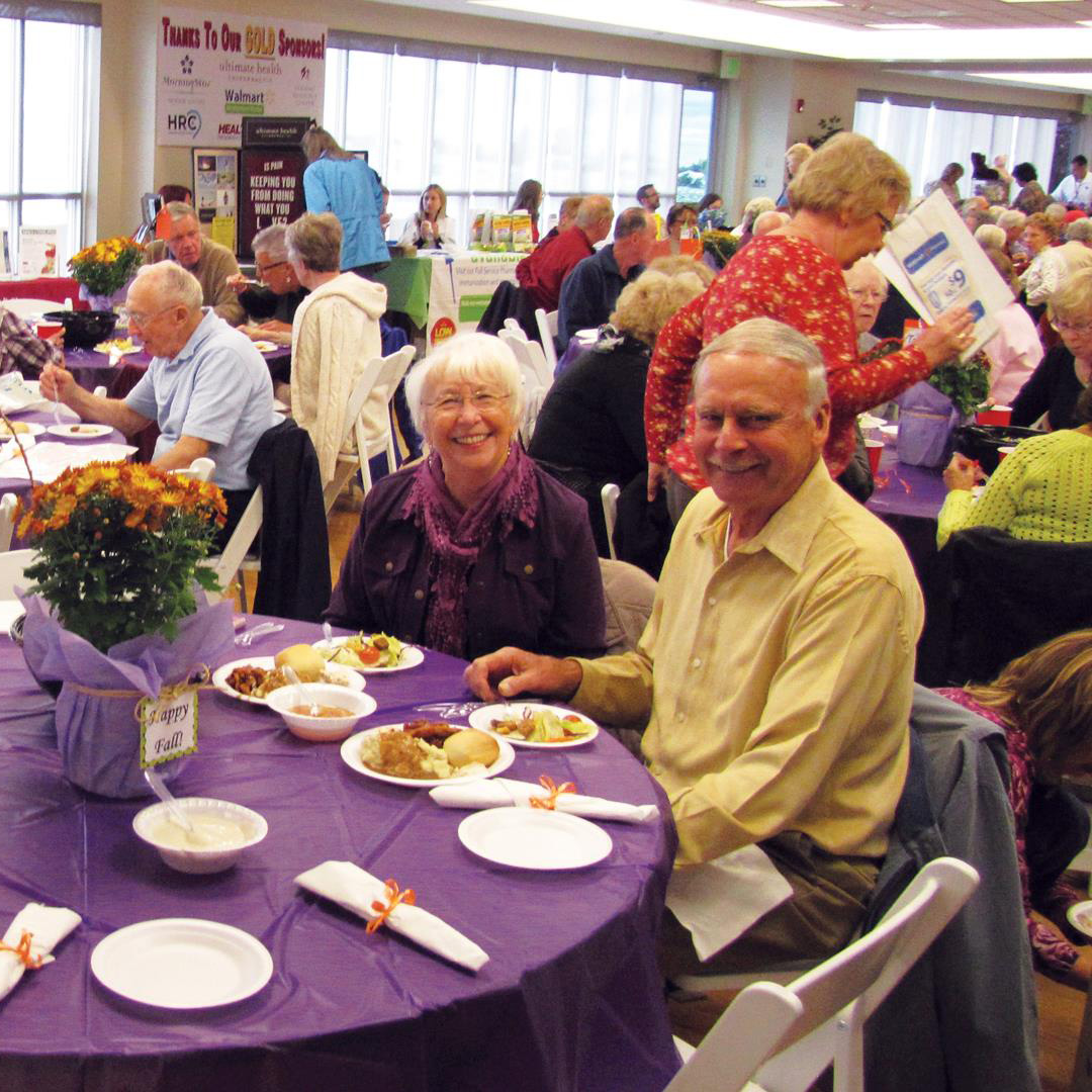 A couple smiling while sitting at banquet tables enjoying lunch.