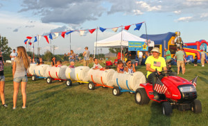 Children riding in a barrel train at an event.