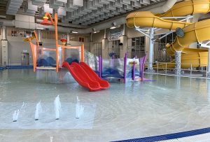 A pool with a playscape, large slide and water features in Ridge Recreation Center's activity pool.