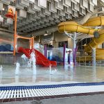 Play feature in the Activity Pool inside Ridge Recreation Center showing colorful apparatuses and slides with the large, yellow flume slide in the background.