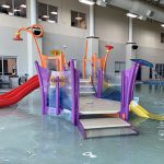 Play feature in the Activity Pool inside Ridge Recreation Center showing colorful apparatuses and slides.