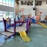 Play feature in the Activity Pool inside Ridge Recreation Center showing colorful apparatuses and slides.