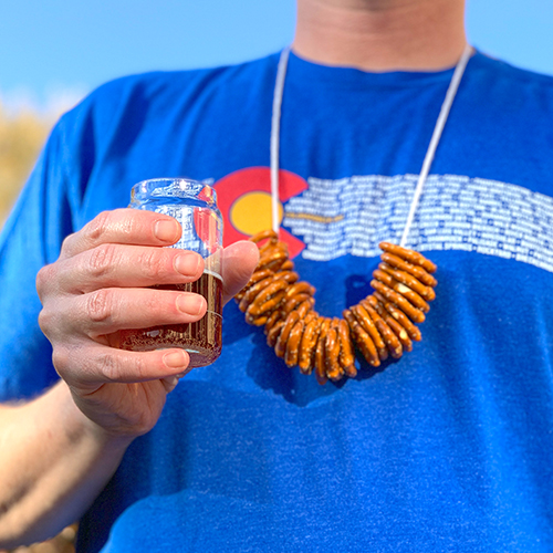 Man attending a beer festival wearing a pretzel necklace and holding a beer tasting glass.