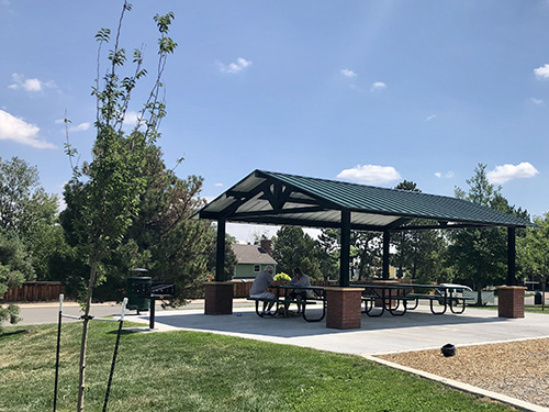 View of the park shelter in Chaucer Park showcasing a new tree planting and two people sitting under the shelter.