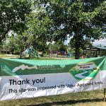 Thank you banner hung at the entrance of Chaucer Park with the park shelter and playground in the background.