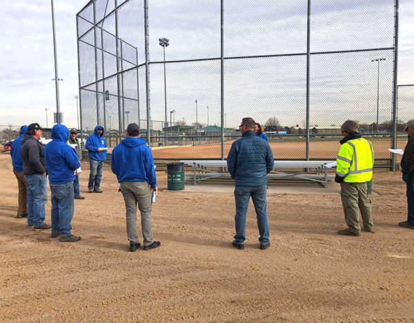 A group of parks staff members standing near a ball field discussing tasks for the day.
