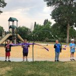 Four children cutting a ribbon gathered in front of the Lilley Pad Park playground for the grand opening.