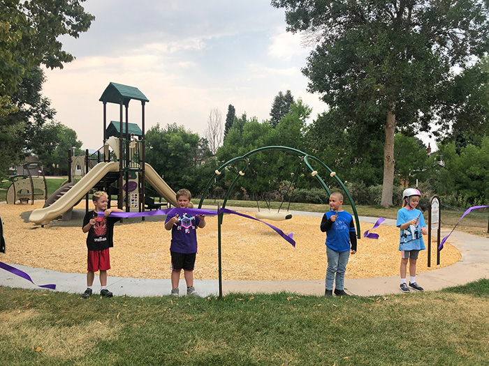 Four children cutting a ribbon gathered in front of the Lilley Pad Park playground for the grand opening.