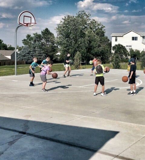 A group of kids outdoors on a basketball court learning to dribble.