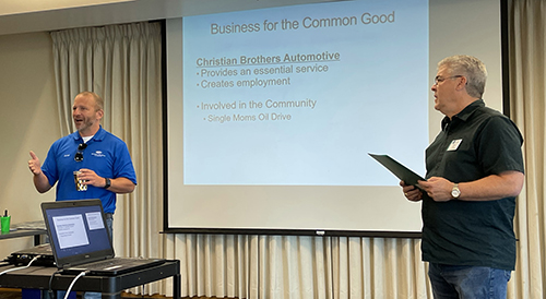 Two men standing in front of a presentation screen discussing the presentation slide.