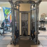 Fitness weight lifting machine with exercise bikes and stair climbers and a colorful mural on the wall in the background.