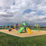 Full playground area with sports fields and a park shelter nearby in the background.