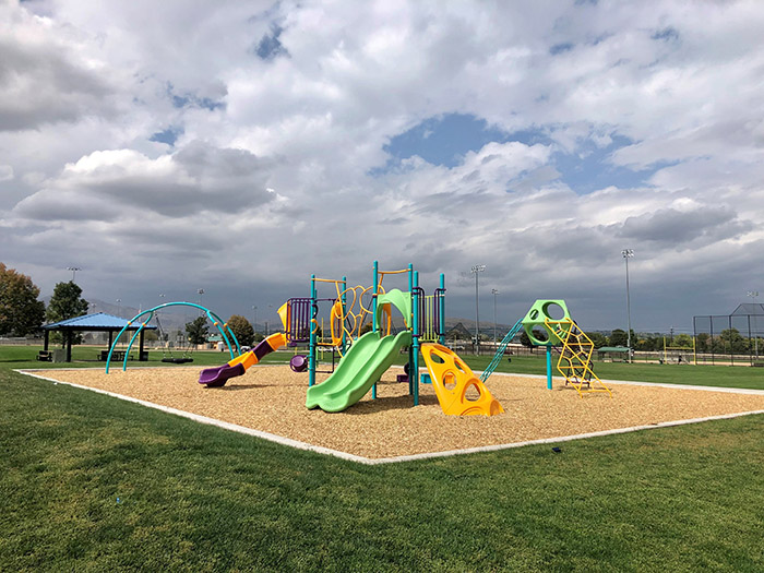 Full playground area with sports fields and a park shelter nearby in the background.