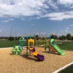 Pieces of playground equipment with sports fields nearby in the background.