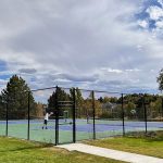 Two tennis courts with fencing around it being used by tennis players.