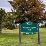 Entry sign for Woodmar Square Park with large trees in the background.