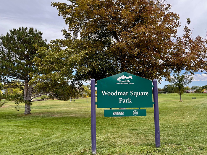 Entry sign for Woodmar Square Park with large trees in the background.