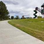 Sidewalk view leading to the playground showcasing a spiral slide on a treehouse looking play feature in Woodmar Square Park.