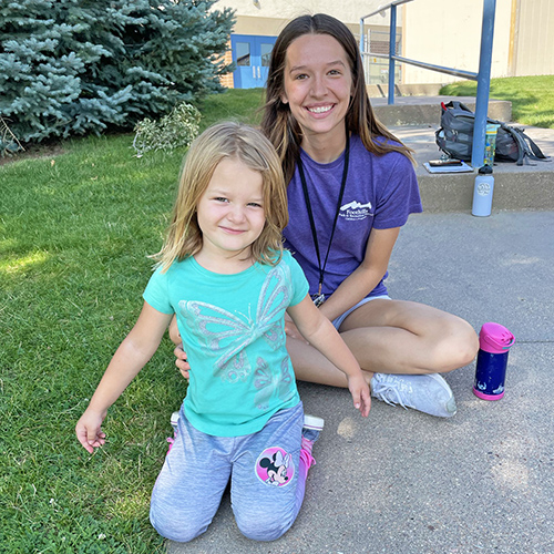 November 17 Job Fair 2021 Summer Camp Leader posing with a smiling, little girl.