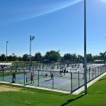 View of the full pickleball and tennis court complex with people playing both sports on all courts.