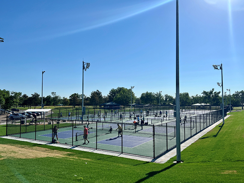 View of the full pickleball and tennis court complex with people playing both sports on all courts.