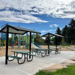 Two new park shelters with picnic tables, new stone seating wall and playground in the background.