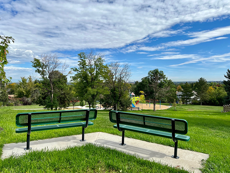 Park benches appointed on top of a hilly slope overlooking the playground.