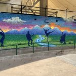 Colorful, painted wall showing the sun setting behind the mountains with various silhouettes of dancers and musicians