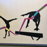 A section of the artworking showing two gymnast silhouettes with a colorful ribbon across their bodies reading the words commitment and strive