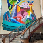 A colorful art mural showcasing different aspects of indoor and outdoor recreation with features like mountains, a swimmer, a basketball player, trees, birds, children holding hands and a heart.