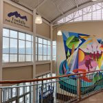 A colorful art mural showcasing different aspects of indoor and outdoor recreation with features like mountains, a swimmer, a basketball player, trees, birds, children holding hands and a heart.