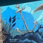 Close up of a section of an art installation on the outside of a building displaying an underwater scene with an anchor and the artist's signature
