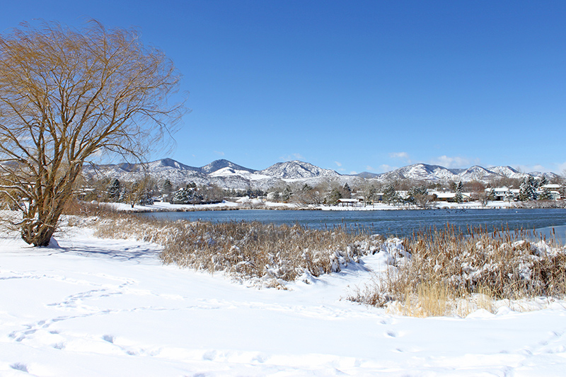 Snowy scene of Beers Sisters Reservoir in Blue Heron Park with snowy mountains in the background
