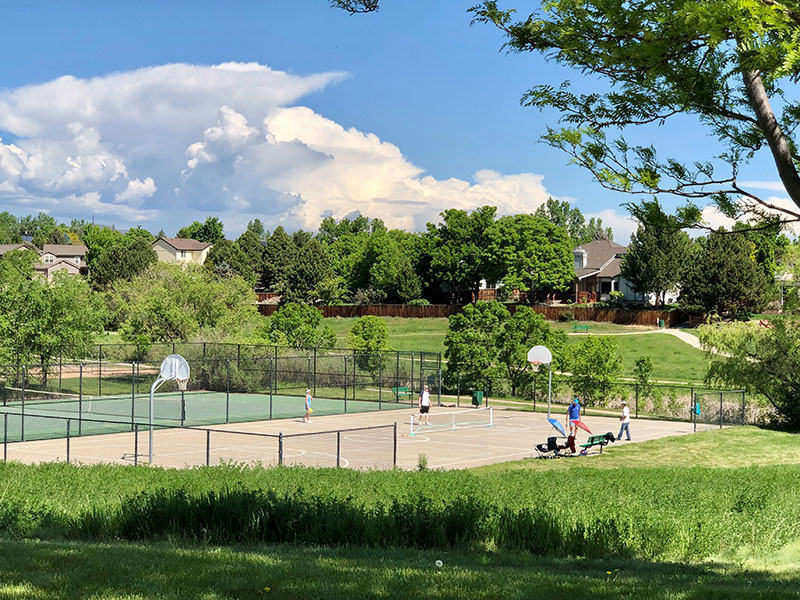 A view looking down onto a basketball court and tennis court being utilized by a group of pickleball players