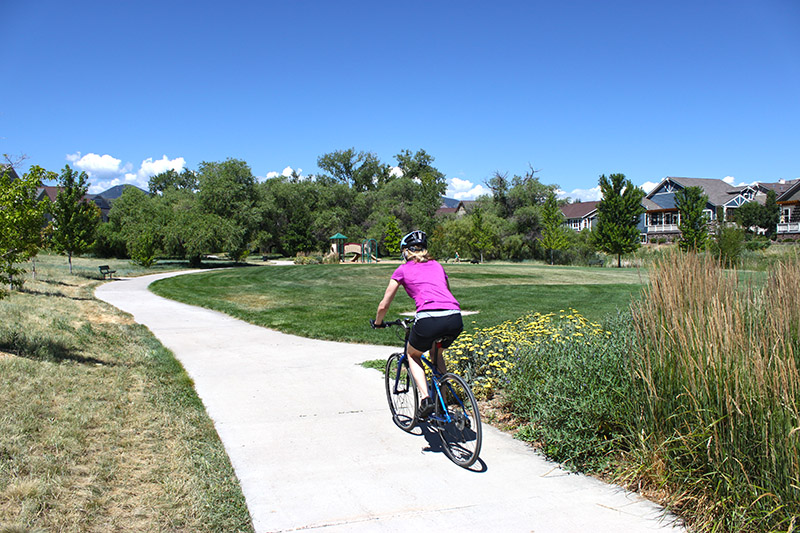 Woman riding a bike on a sidewalk in Dancing Willows Park.