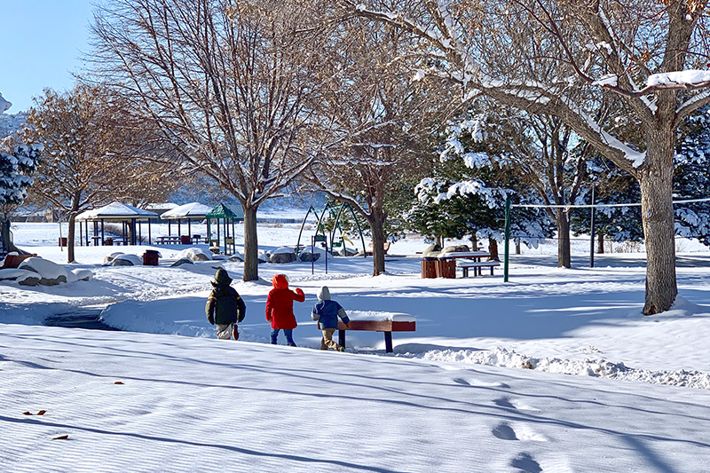 Eason Regional park in snow with three children bundled up for snowy weather walking on a plowed sidewalk.