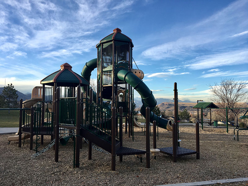 A playground with slides and climbing apparatuses with a picnic shelter and mountainous views in the background