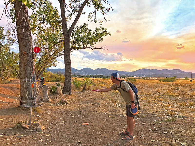 A man playing disc golf putts to the basket during sunset behind the mountains in Fehringer Ranch Park