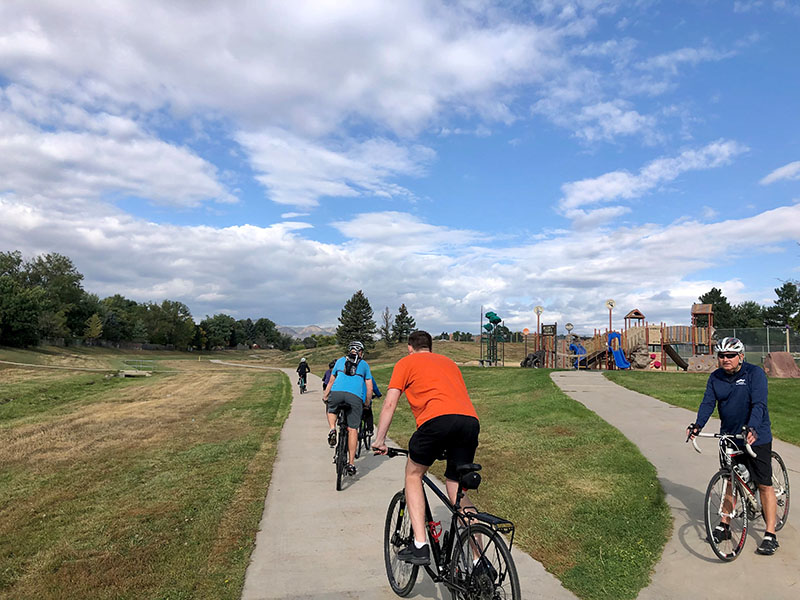 A cement trail showing a group of bike riders and a Colorado themed playground in the background