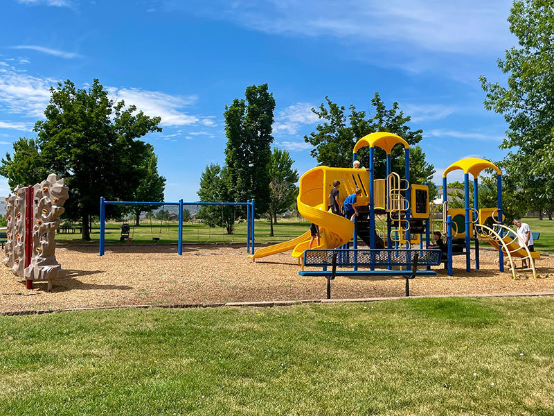 Playground with blue and yellow play features, swing set, climbing wall and a park bench