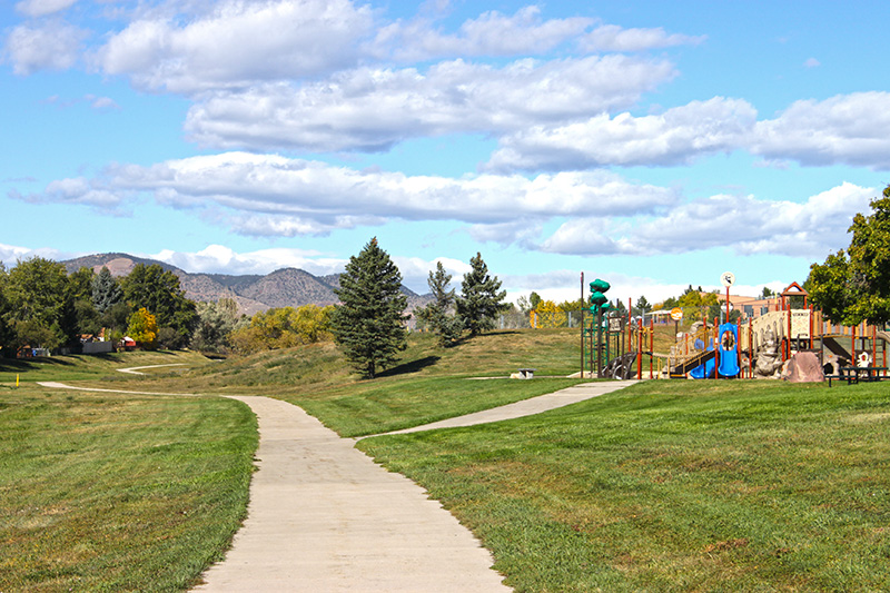 A long trail with mountains in the background with a sidewalk leading to a playground