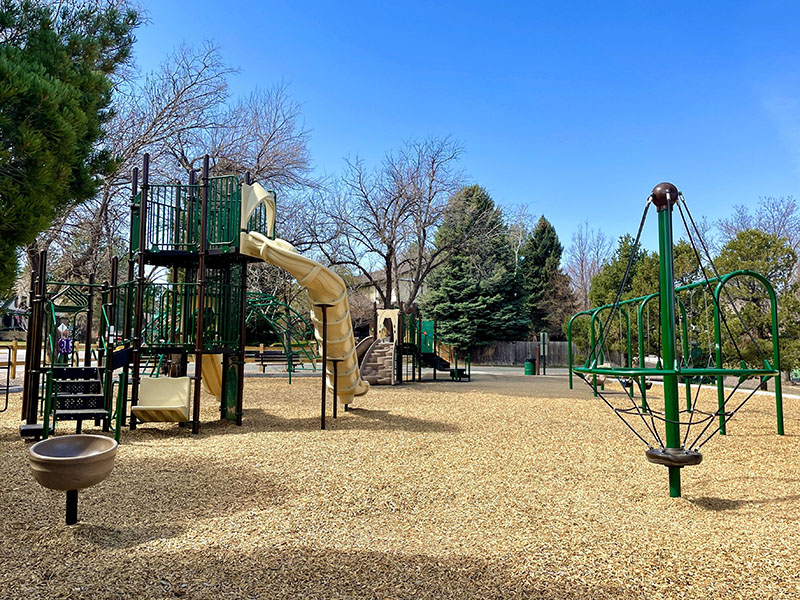 A playground with several climbing features and slide, swing set and spinner